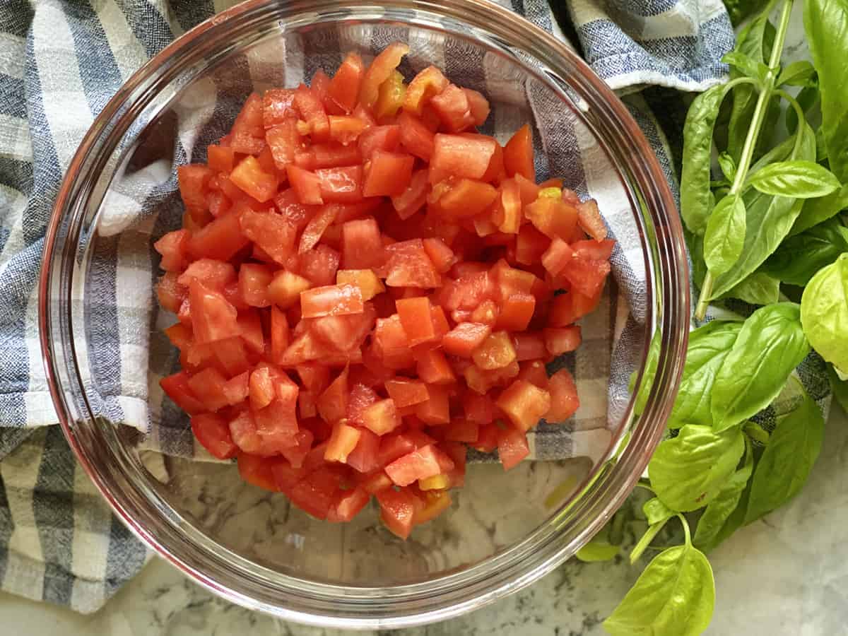 Freshly diced Roma tomatoes sitting in a stainless steel mixing bowl on a kitchen counter