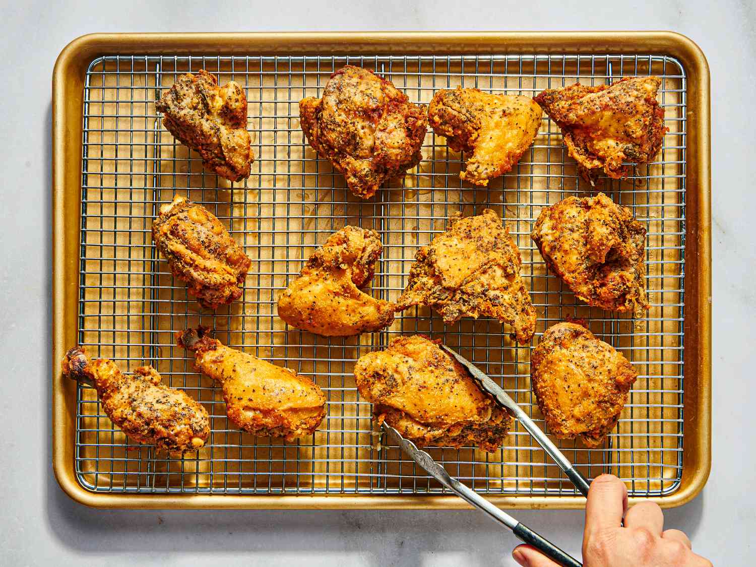 Freshly fried chicken pieces resting on a wire rack set over a baking sheet to drain