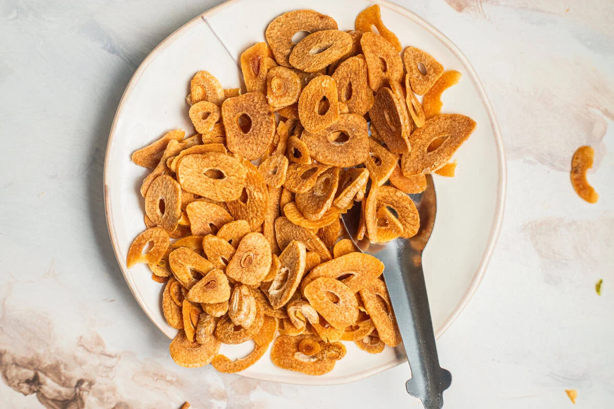 Freshly fried garlic chips draining on a paper towel on a plate
