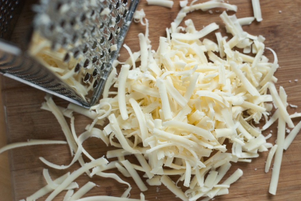 Freshly shredded white American cheese piled on a plate on a kitchen counter, ready for melting