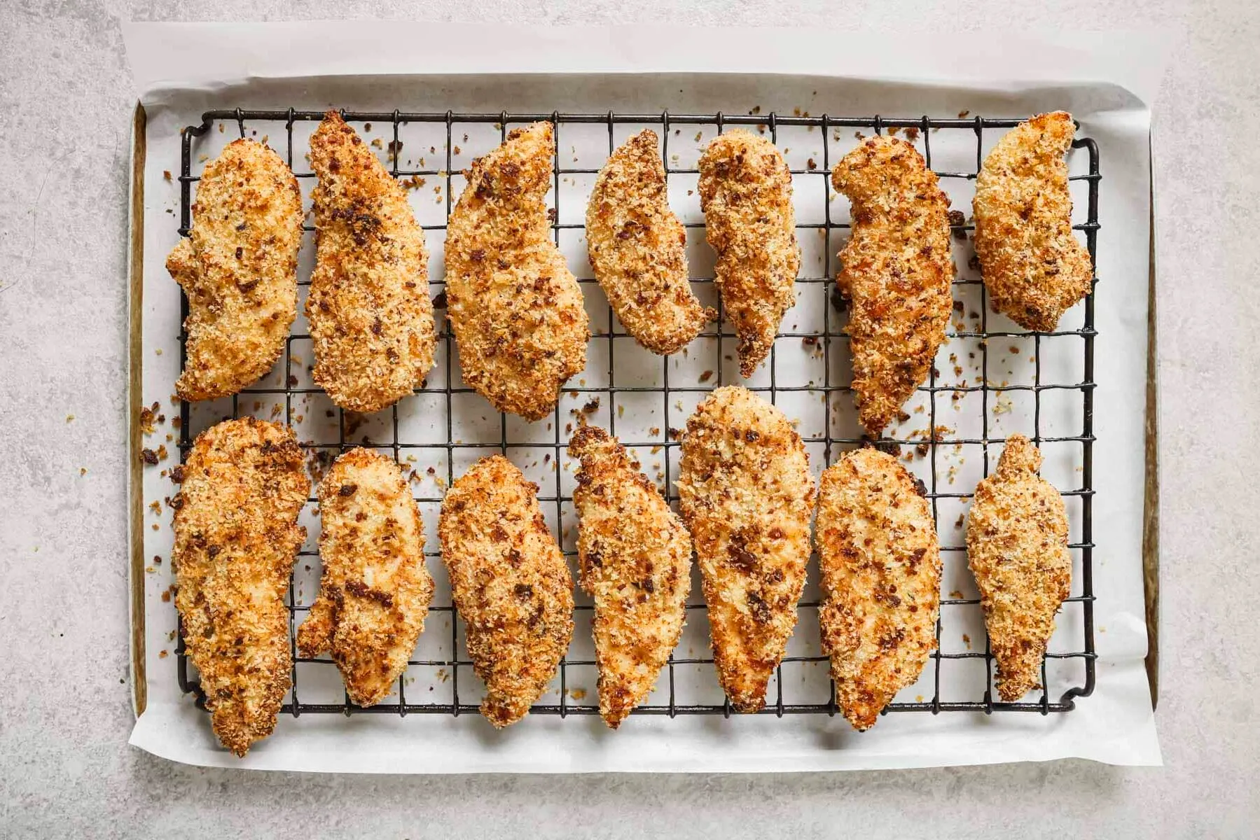 Fried chicken tenders cooling on a wire rack set over a sheet pan on a kitchen counter
