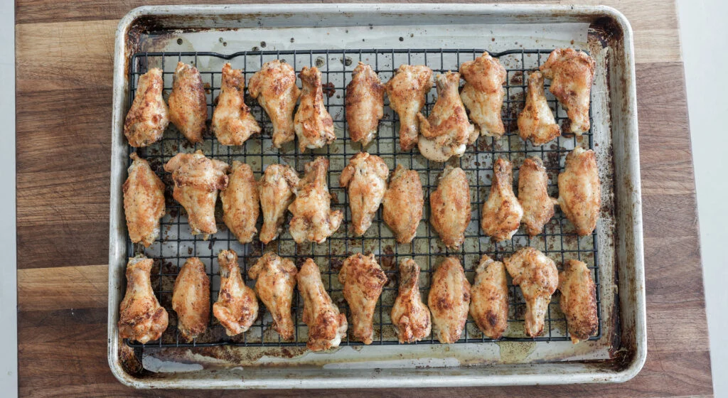Fried chicken wings arranged on a wire rack over a sheet pan inside an oven, mid reheat
