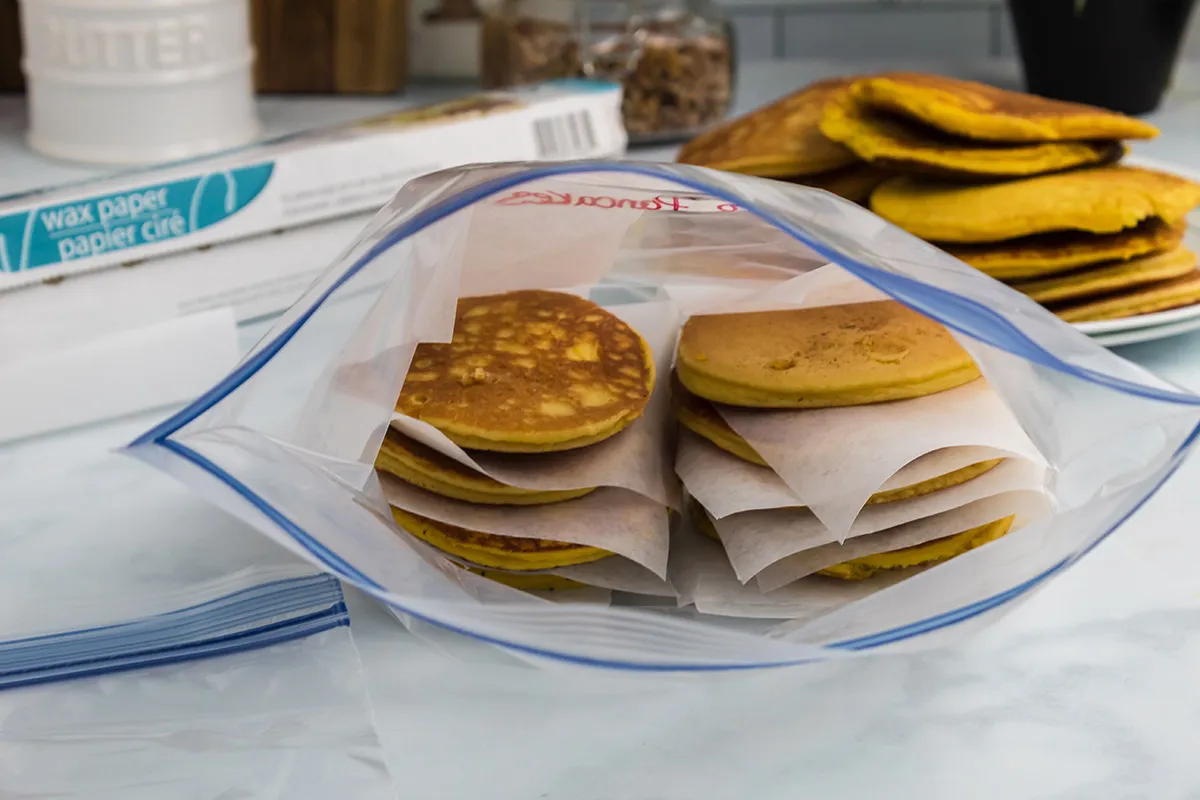 Frozen banana pancakes stacked in a clear freezer bag on a kitchen counter with a parchment sheet between layers