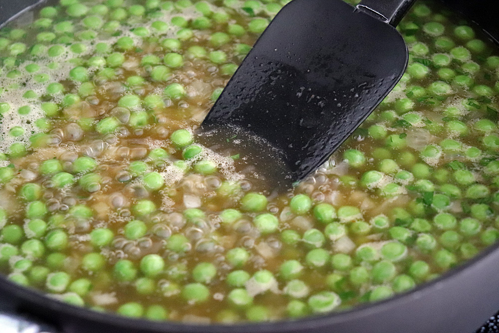 Frozen peas briefly boiling in a small saucepan on a stovetop with steam rising