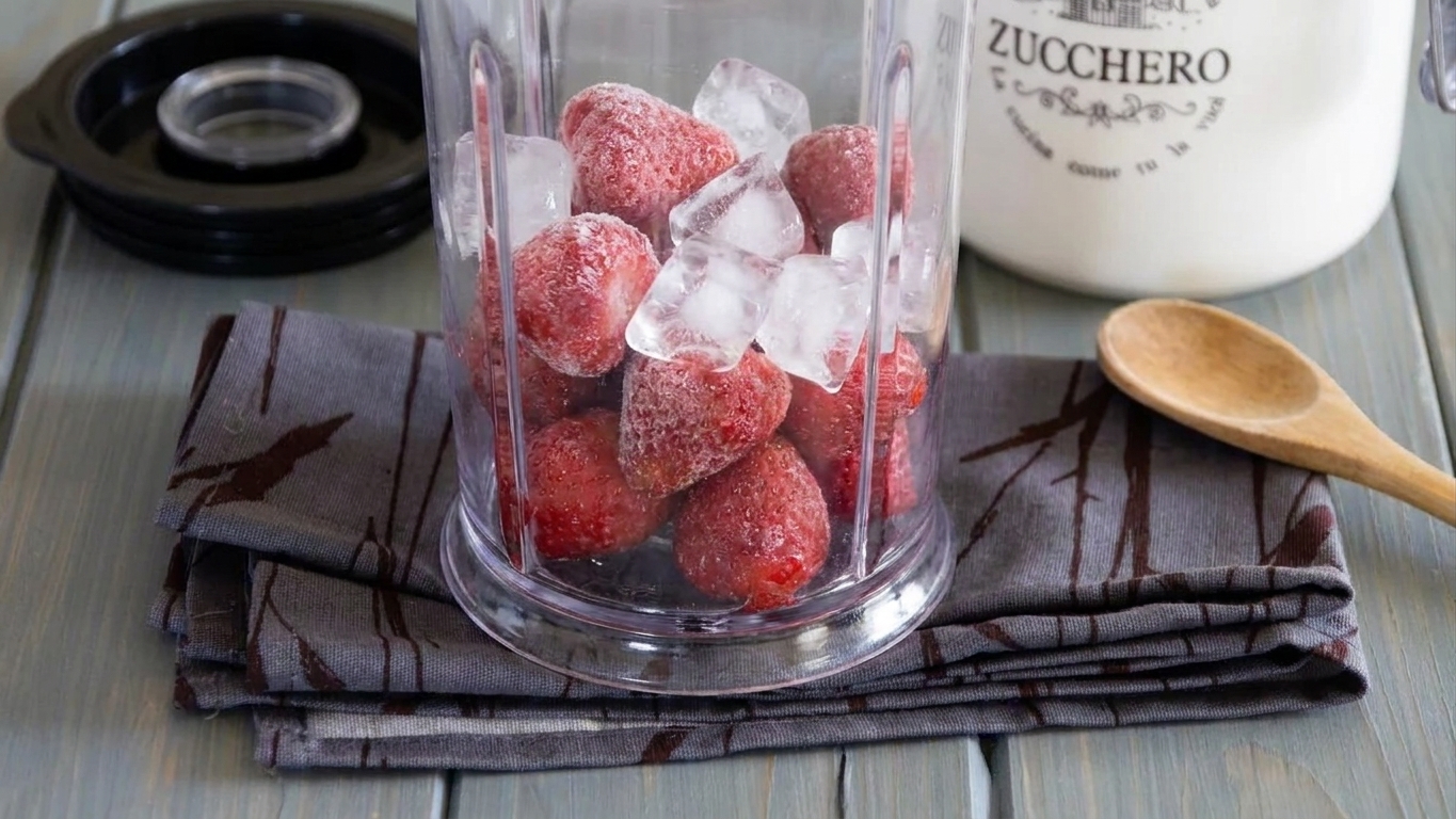 Frozen strawberries and ice inside a blender jar on a kitchen counter before blending