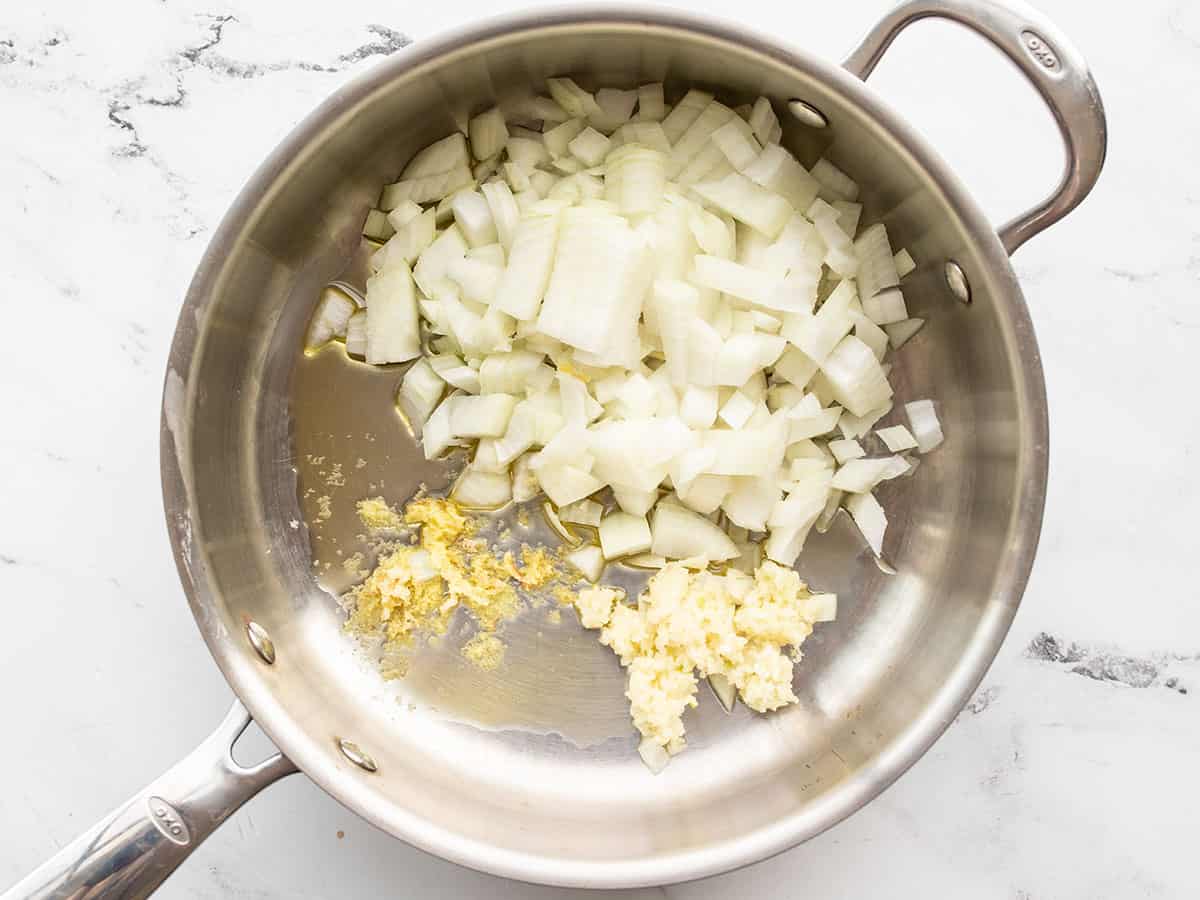 Garlic and grated ginger sizzling in a small saucepan with a little oil on a stovetop, captured mid-cook