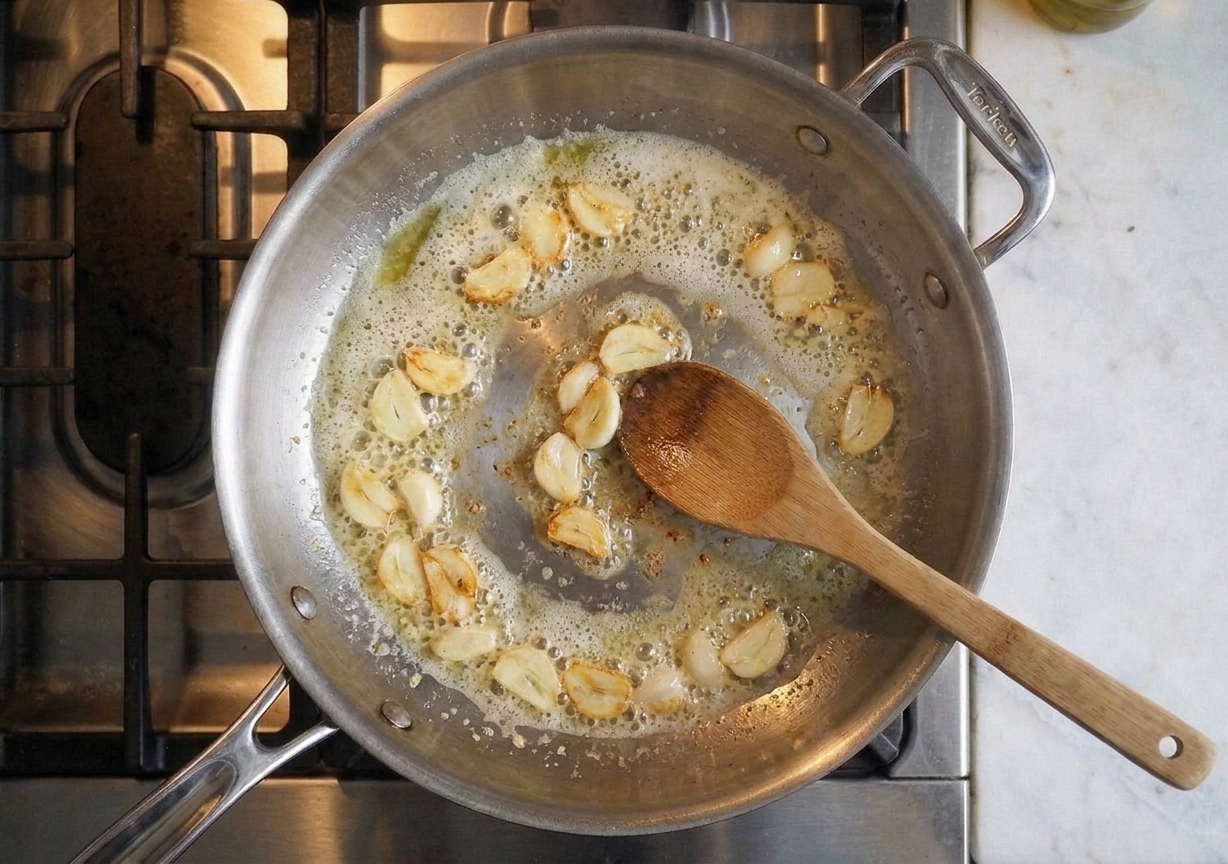 Garlic gently sizzling in melted butter in a skillet on a stovetop