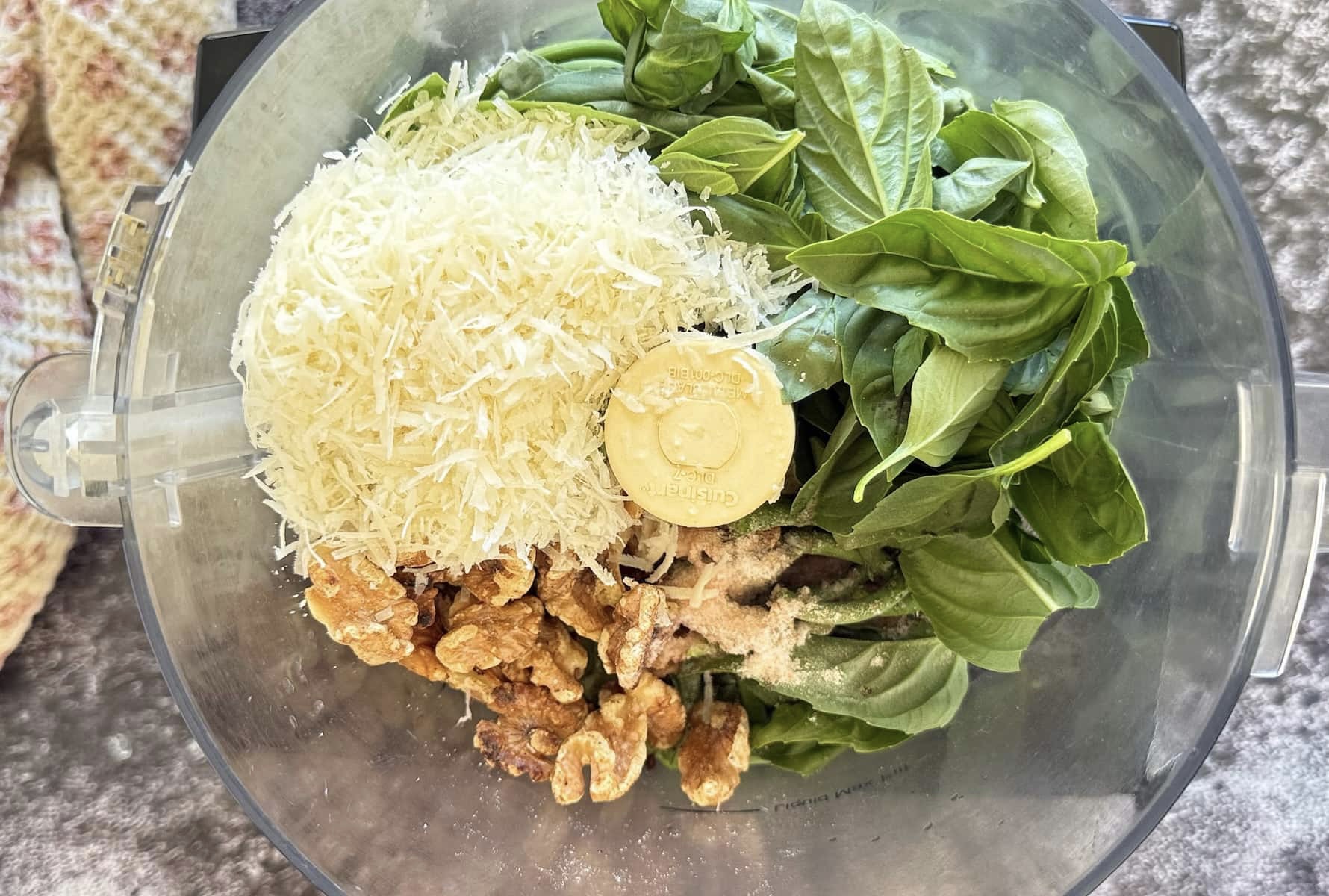 Garlic scapes, fresh basil, grated Parmesan, toasted nuts, lemon, and olive oil arranged on a clean kitchen counter ready for pesto