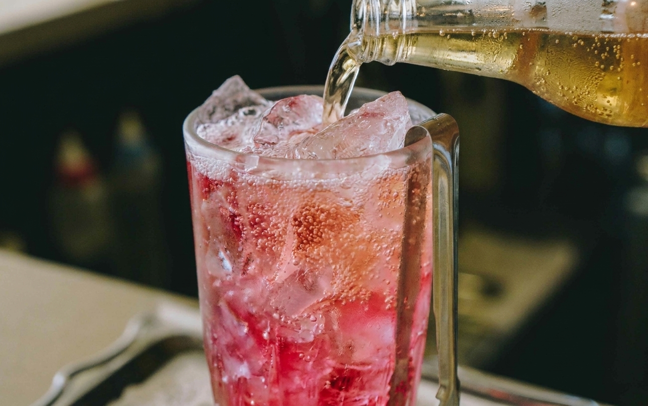 Ginger beer being poured into a pink drink over ice, bubbles rising to the top
