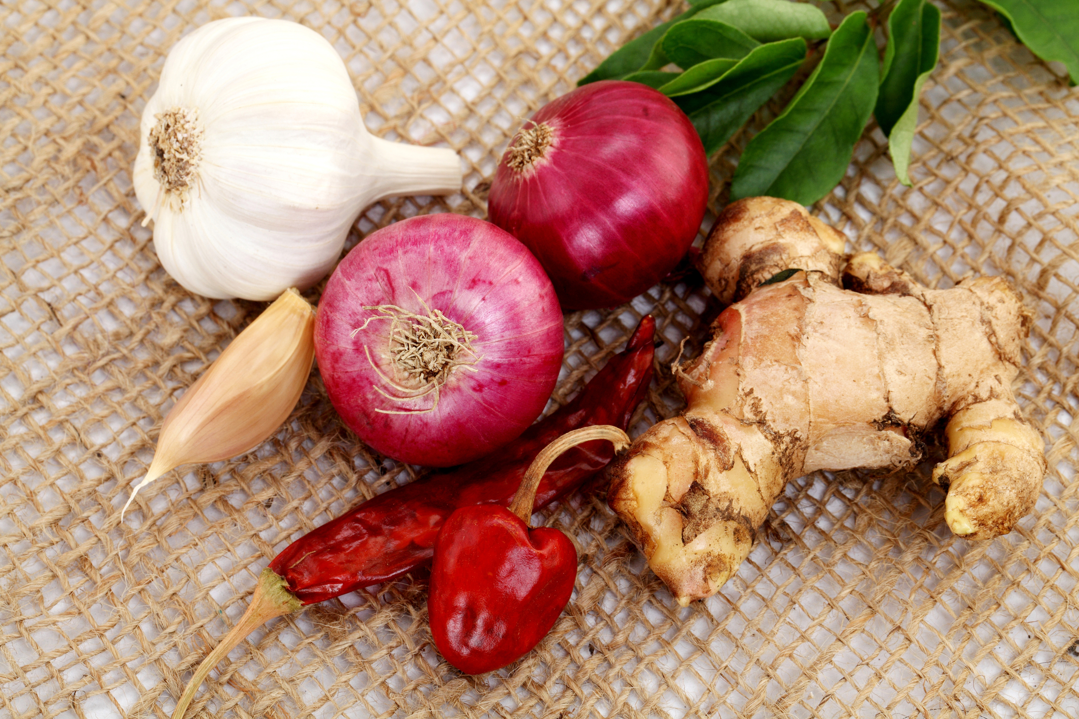 Ginger, garlic, and onion prepped on a wooden cutting board beside a pot on the stove