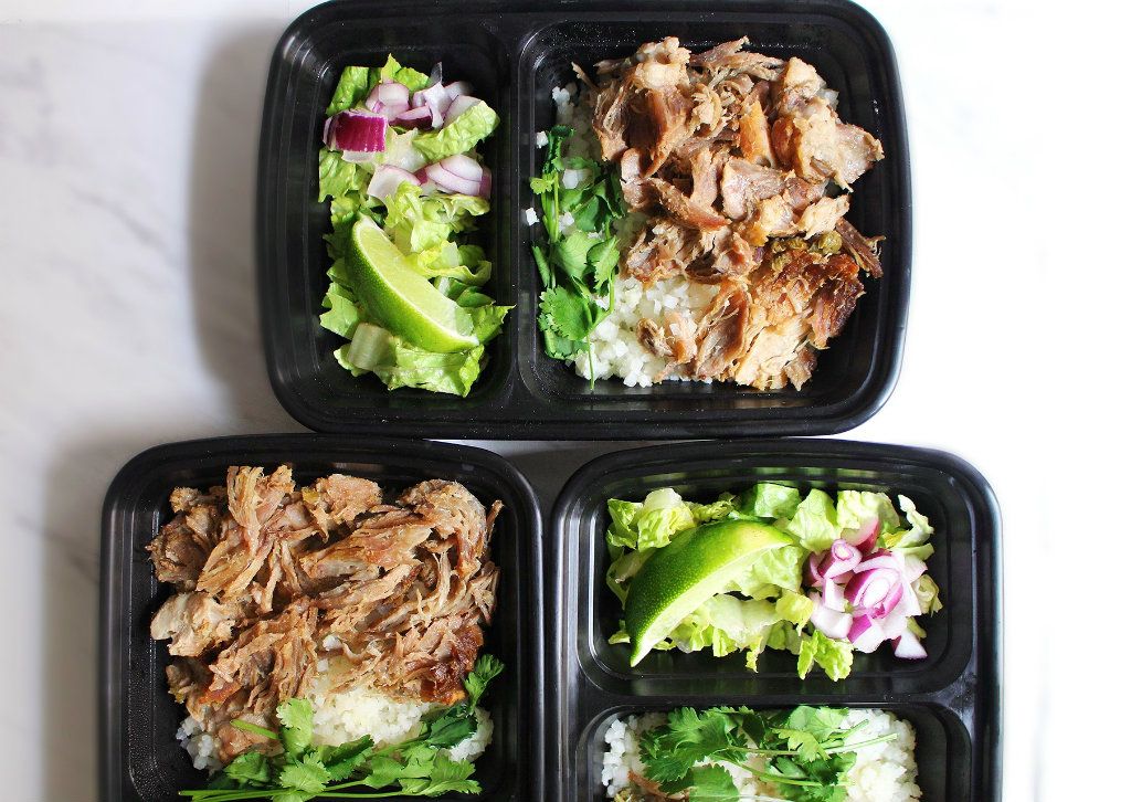 Glass meal prep containers filled with carnitas, cilantro, lime wedges, and rice on a tidy kitchen counter