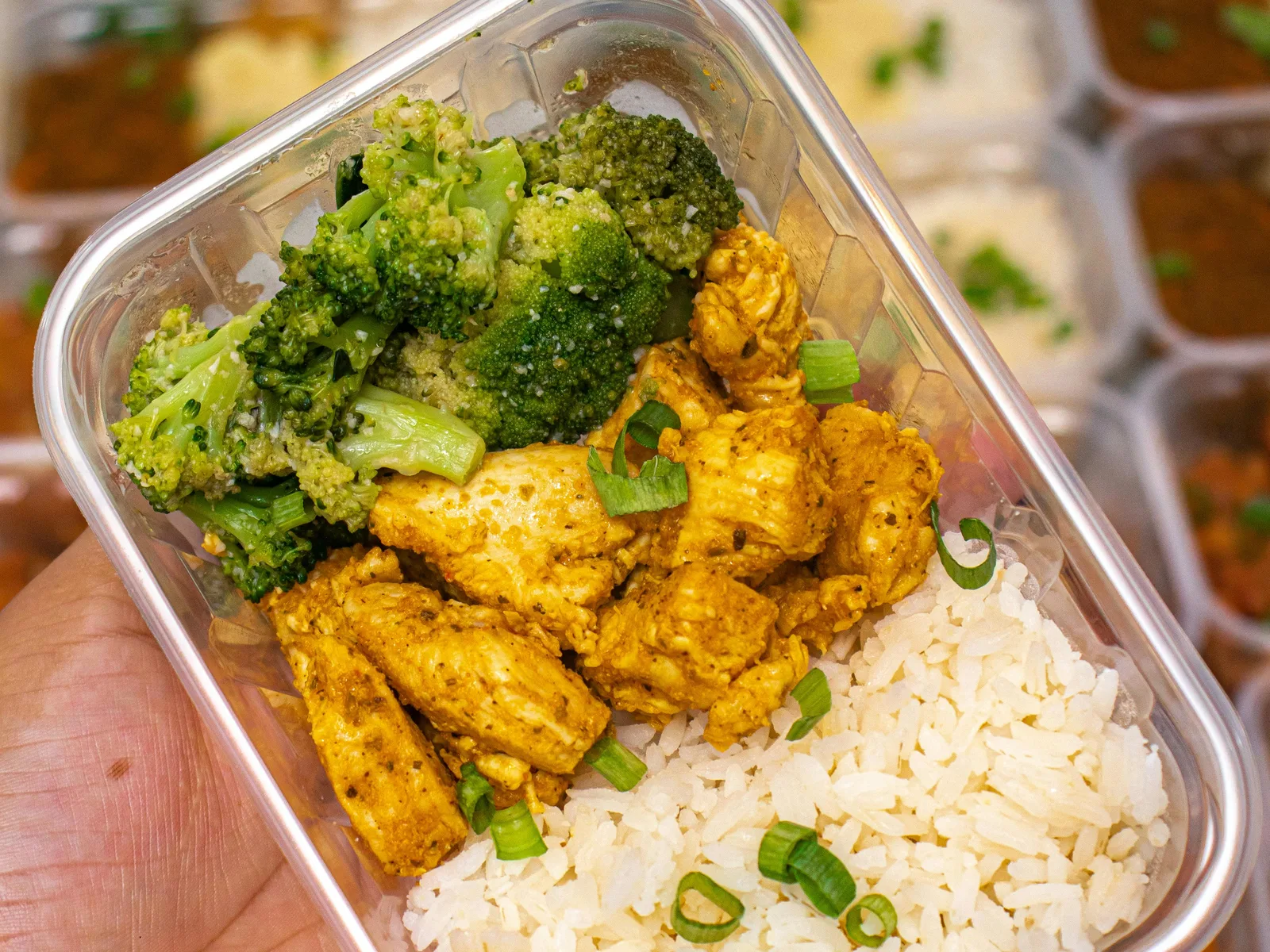 Glass meal prep containers on a kitchen counter holding leftover rice and sliced chicken with a lemon wedge beside them