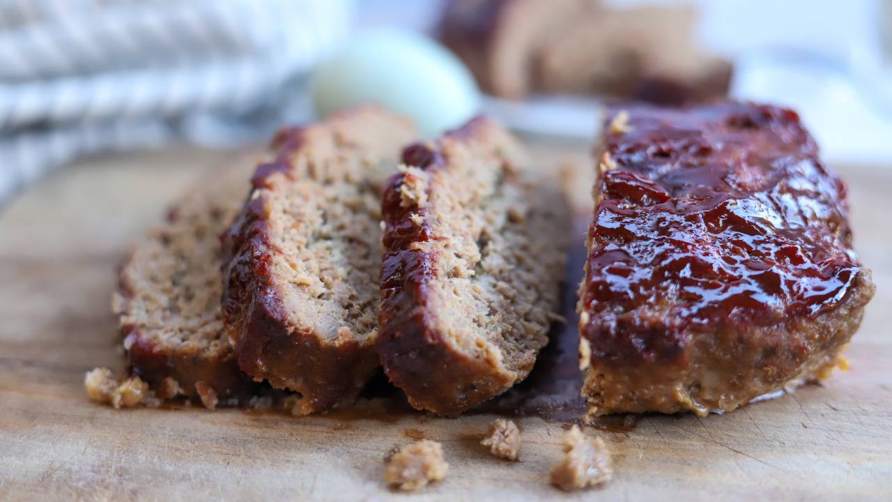 Glossy ketchup-glazed meatloaf sliced thick on a cutting board with a few slices fanned out in warm kitchen light