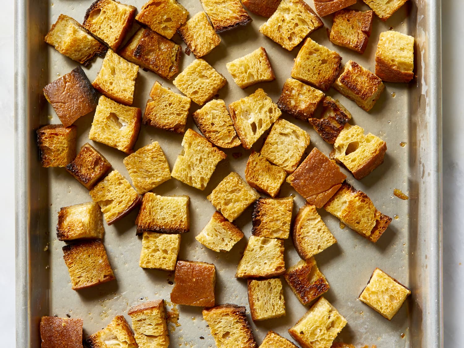 Gluten free bread cubes drying on a rimmed sheet pan in a warm oven