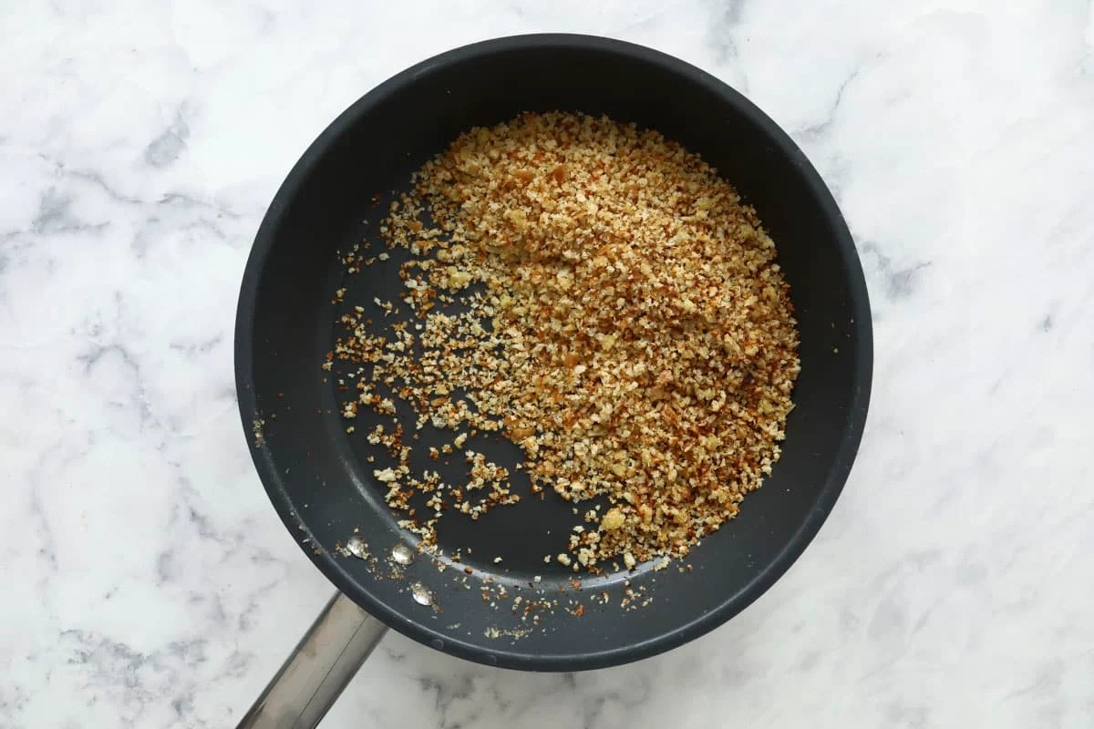 Golden breadcrumbs toasting in a skillet with butter and garlic, shot from above on a stovetop