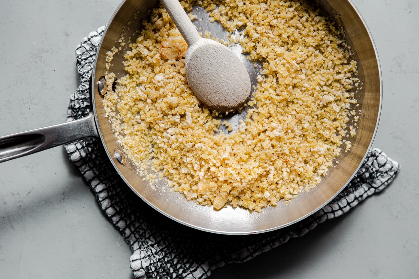 Golden panko breadcrumbs toasting in a skillet with sliced garlic on a stovetop under warm kitchen lighting
