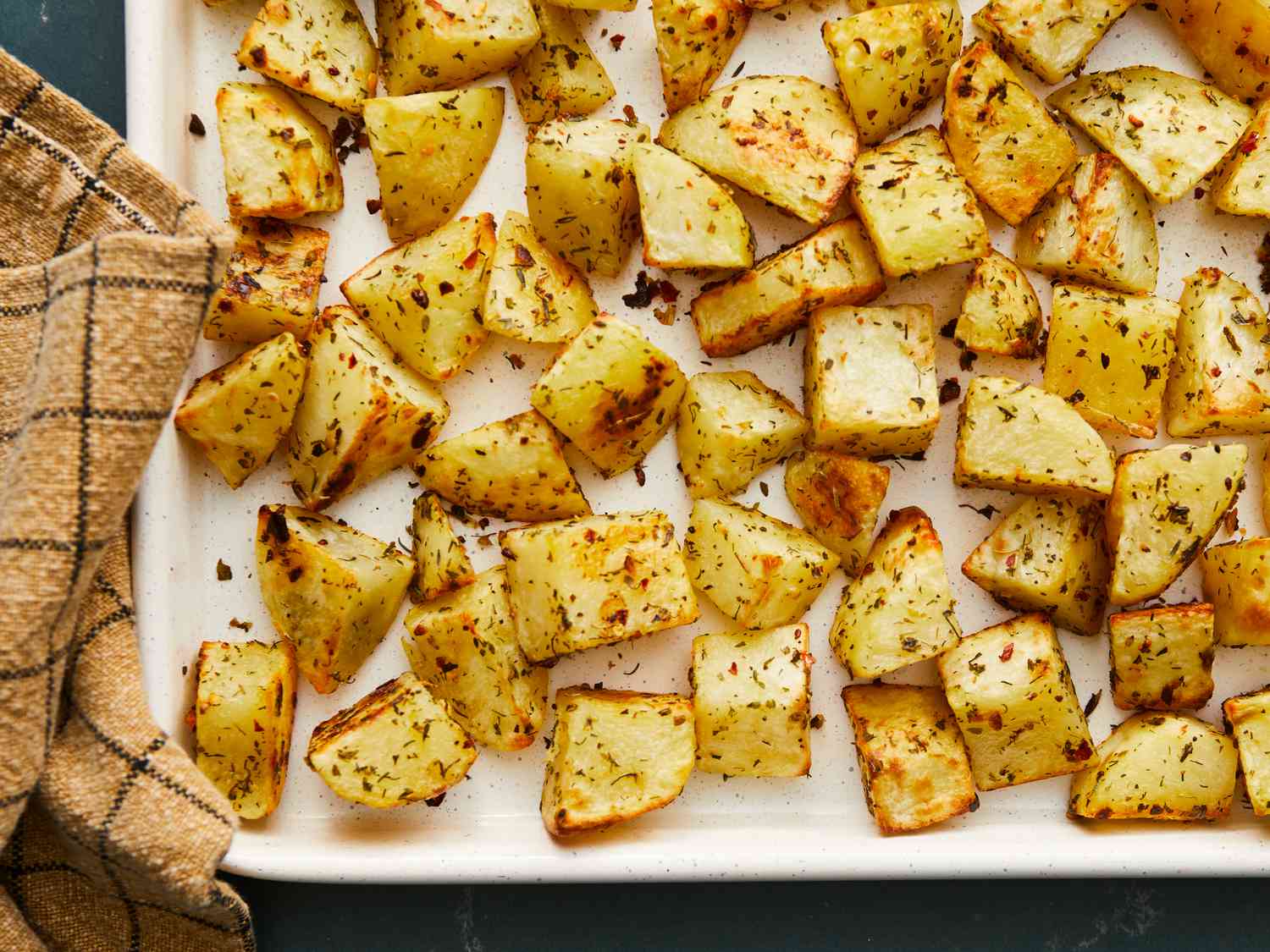 Golden roasted potato cubes spread across a rimmed sheet pan with crisp edges in a home kitchen