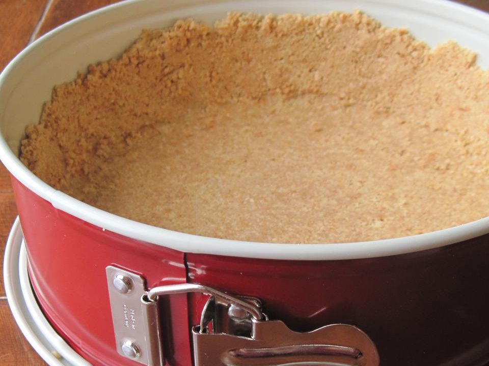 Graham cracker crust pressed evenly into the bottom of a springform pan on a light kitchen counter