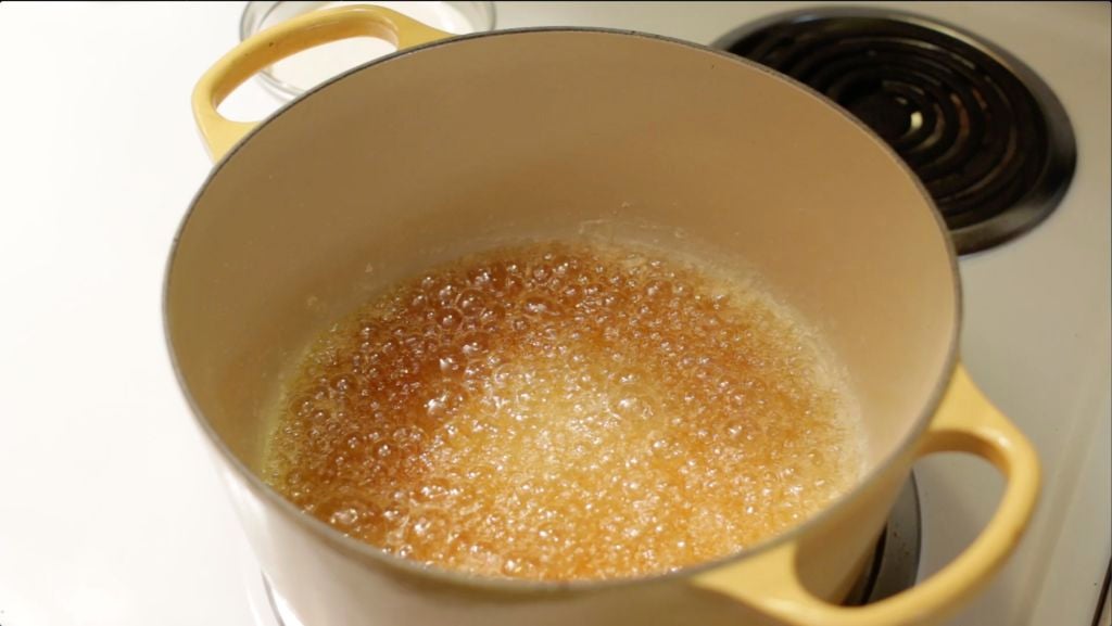 Granulated sugar melting into amber caramel in a small saucepan on a stovetop
