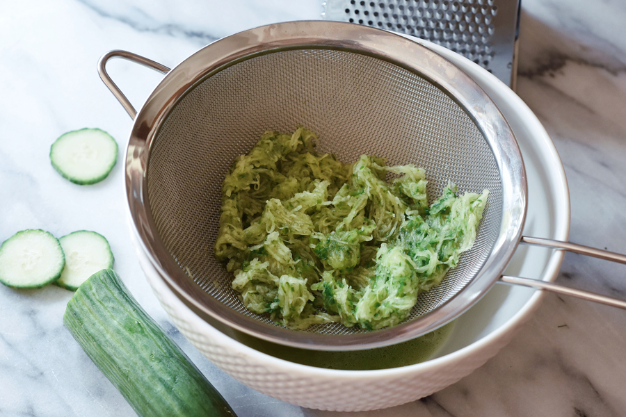 Grated cucumber piled in a clean kitchen towel over a bowl, ready to be squeezed dry