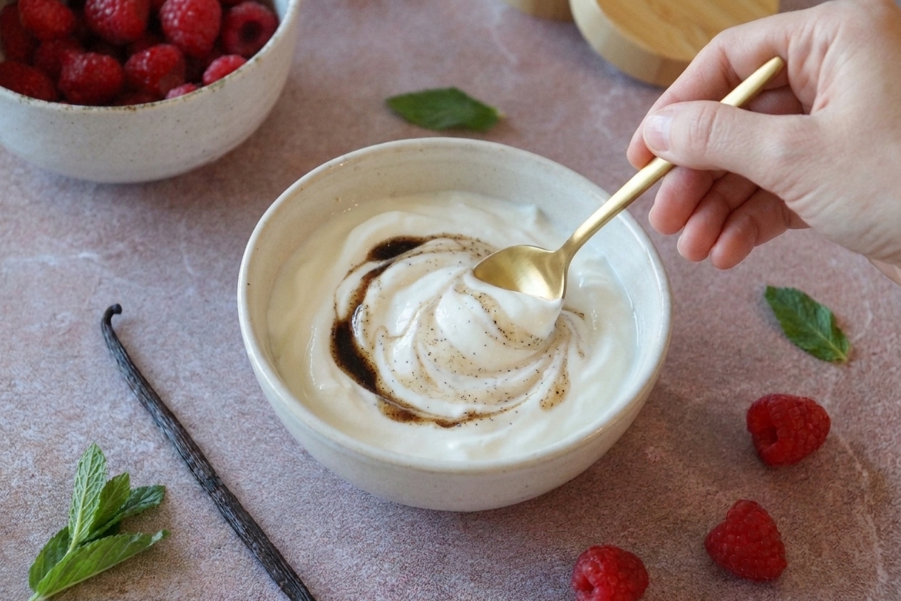 Greek yogurt being stirred with vanilla in a small bowl with a spoon on a stone countertop
