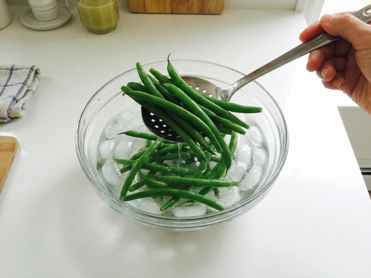 Green beans being lifted from an ice water bath with a slotted spoon on a kitchen counter