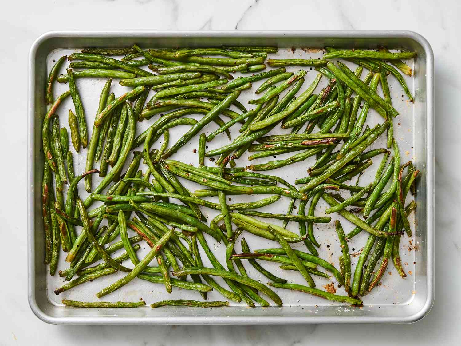 Green beans roasting on a sheet pan in the oven, starting to blister and brown at the edges