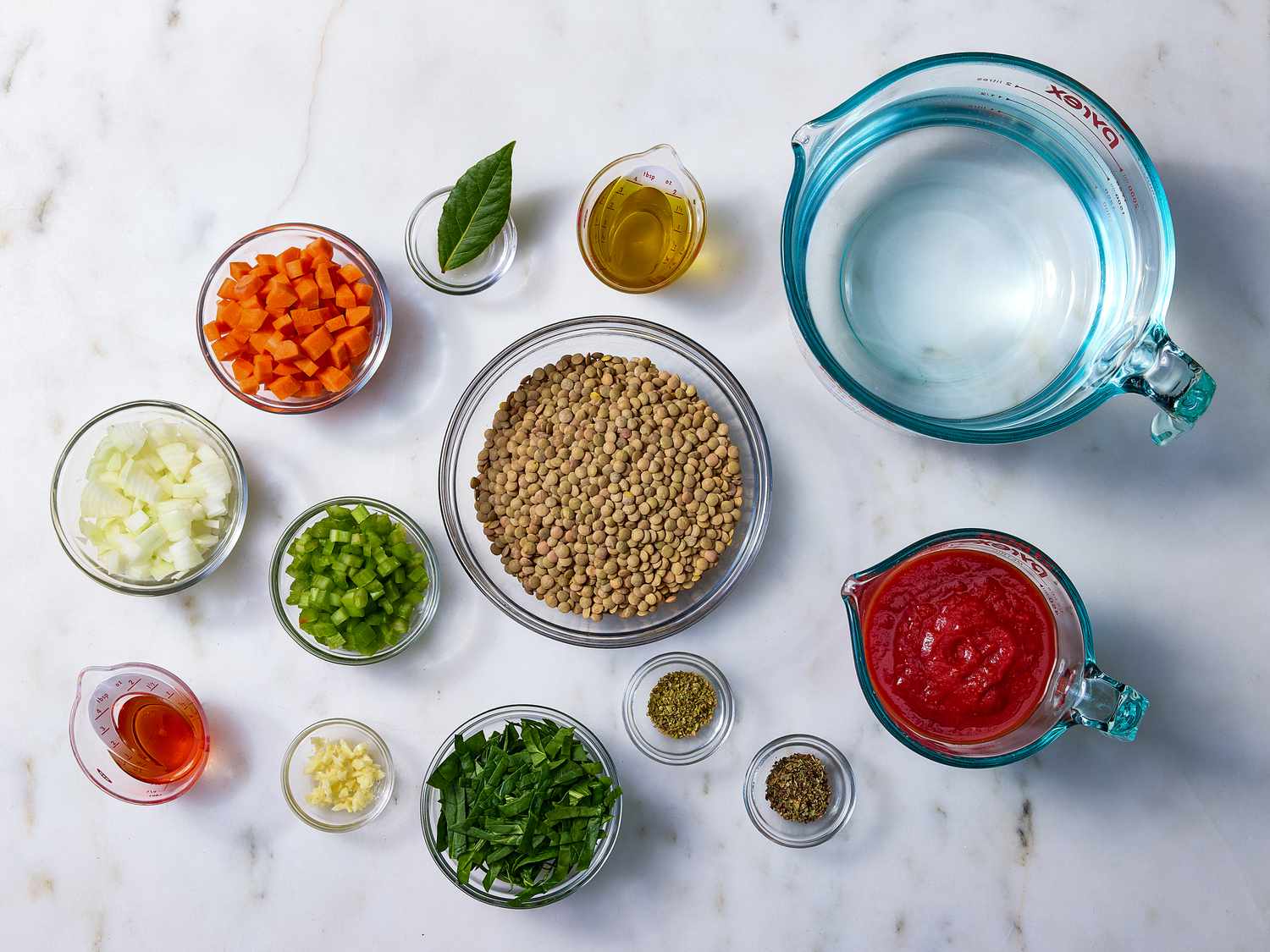 Green lentils, chopped carrots, celery, onion, garlic, lemon, dill, spices, and broth arranged on a bright kitchen counter in small bowls