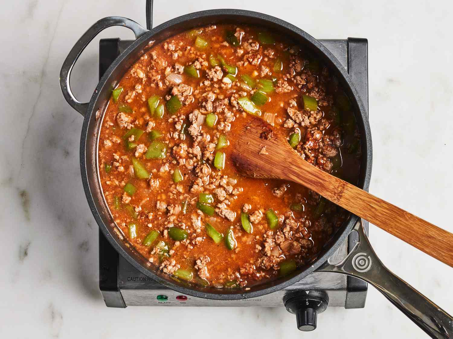 Ground beef, a bottle of ketchup, and a bowl of brown sugar arranged on a bright kitchen counter next to measuring spoons