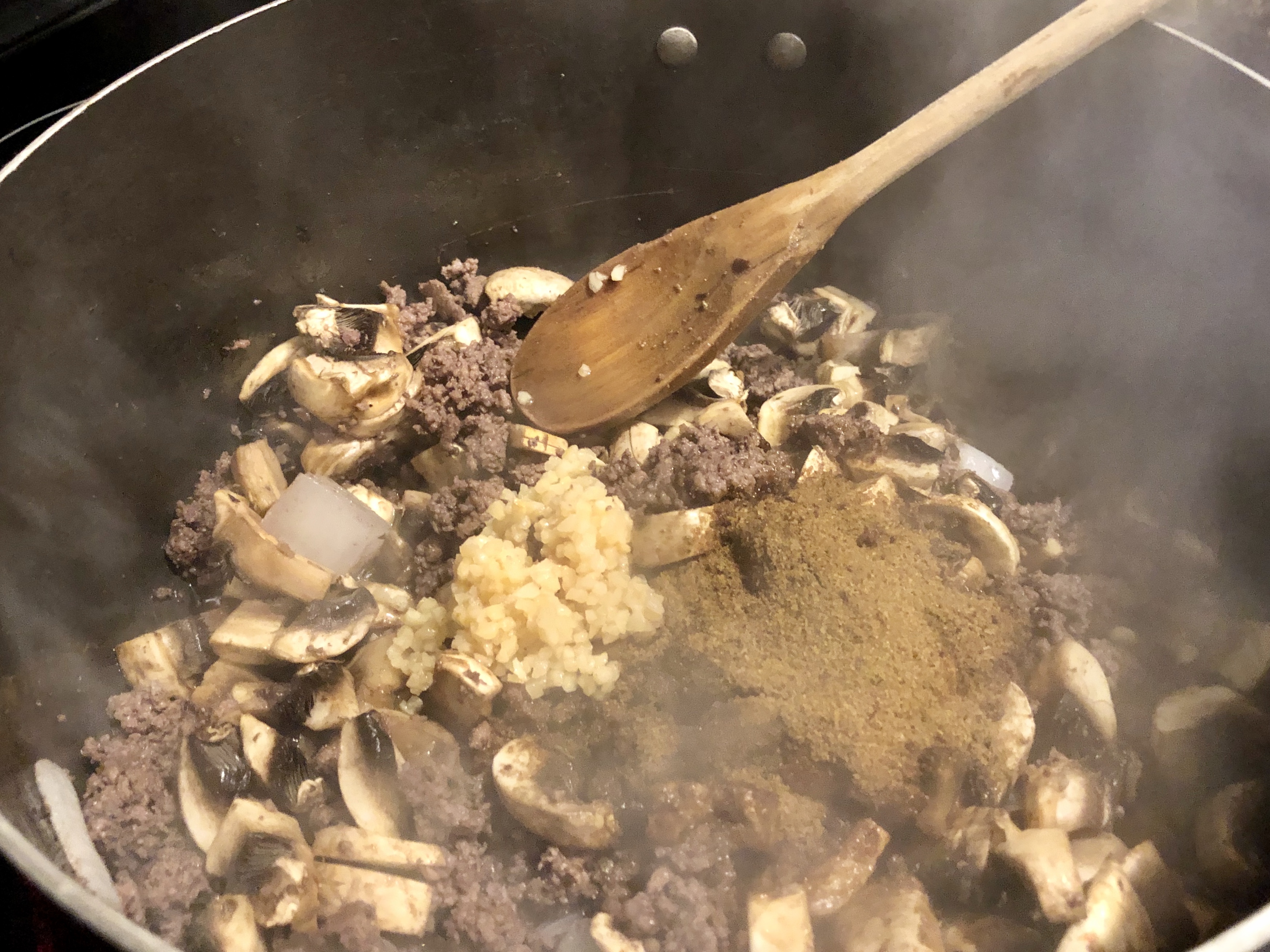 Ground beef and diced onions browning in a large skillet on a stovetop, with a wooden spoon stirring as the meat develops browned bits