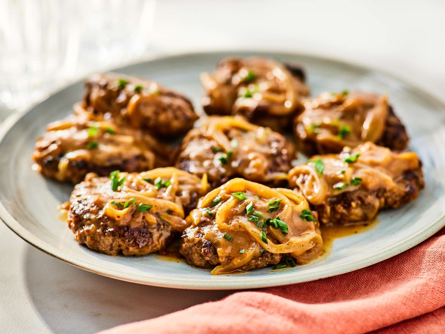 Ground beef and diced onions browning together on a stovetop in a cast iron skillet with a wooden spoon