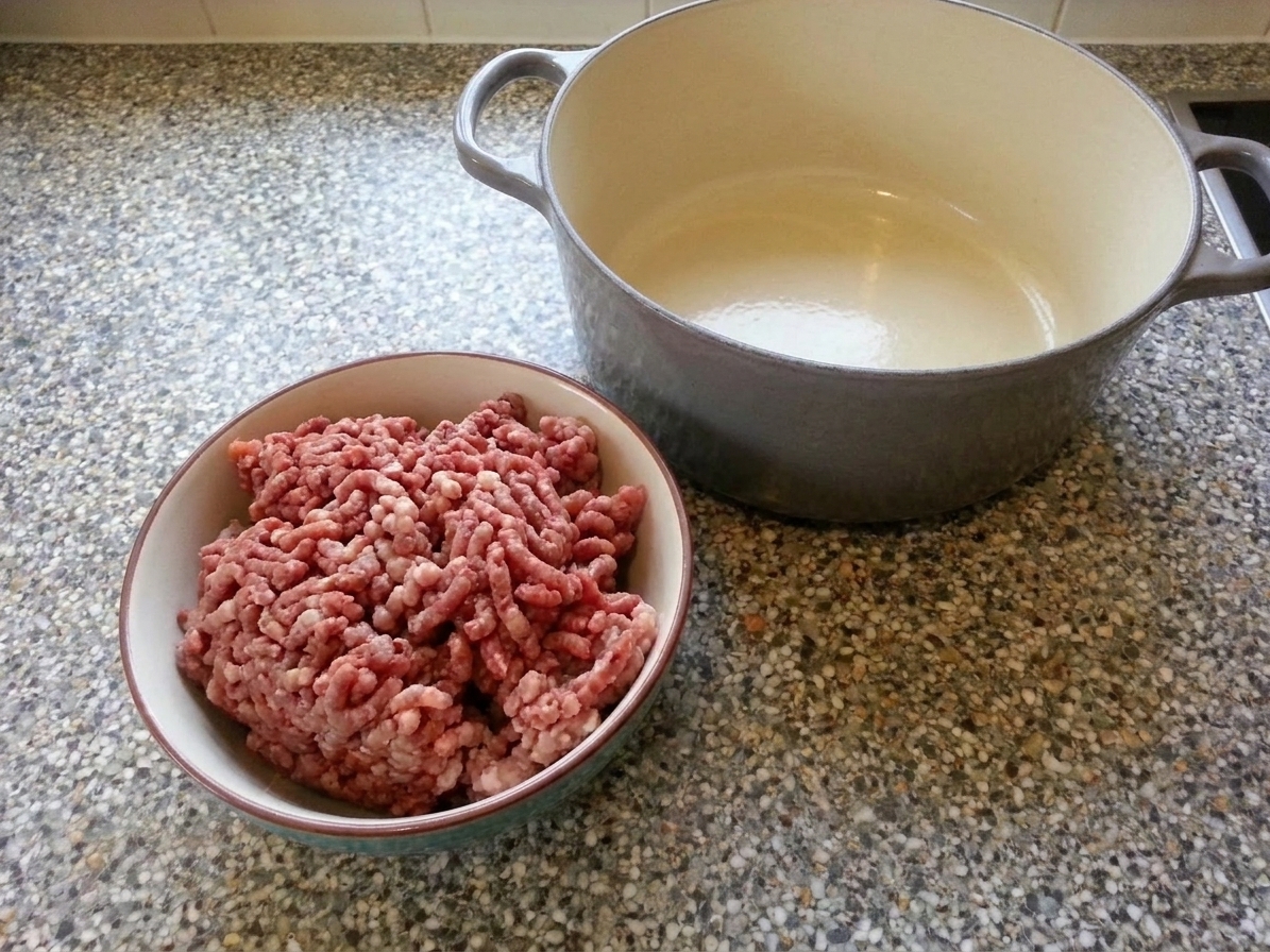 Ground beef and ground pork in a bowl next to a Dutch oven on a kitchen counter, ready to be browned for bolognese