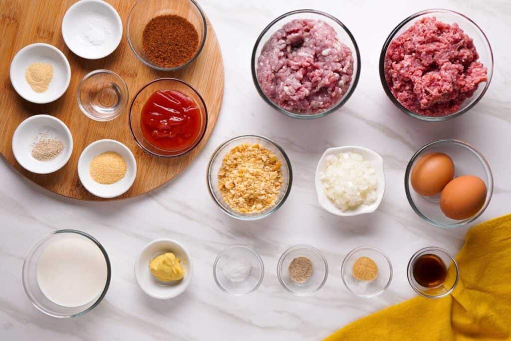 Ground beef, breadcrumbs, eggs, onion, ketchup, Worcestershire sauce, and spices arranged on a kitchen counter, ready for meatloaf prep