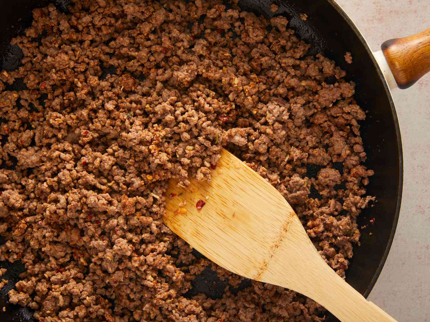 Ground beef browning in a Dutch oven on a stovetop with a wooden spoon breaking it into small crumbles, warm kitchen lighting