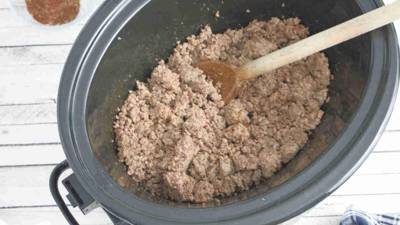 Ground beef browning in a heavy pot on the stovetop with browned bits forming on the bottom