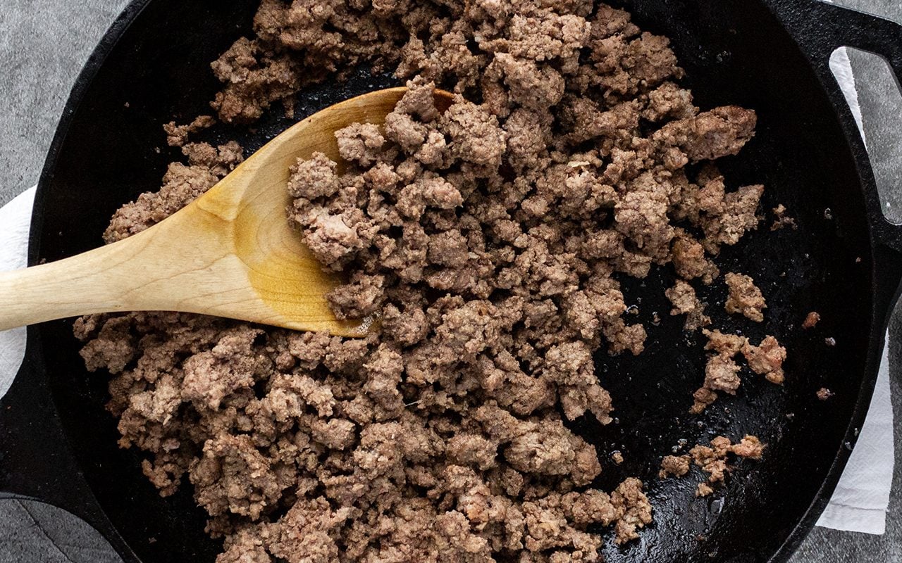 Ground beef browning in a large Dutch oven on a stovetop with a wooden spoon stirring