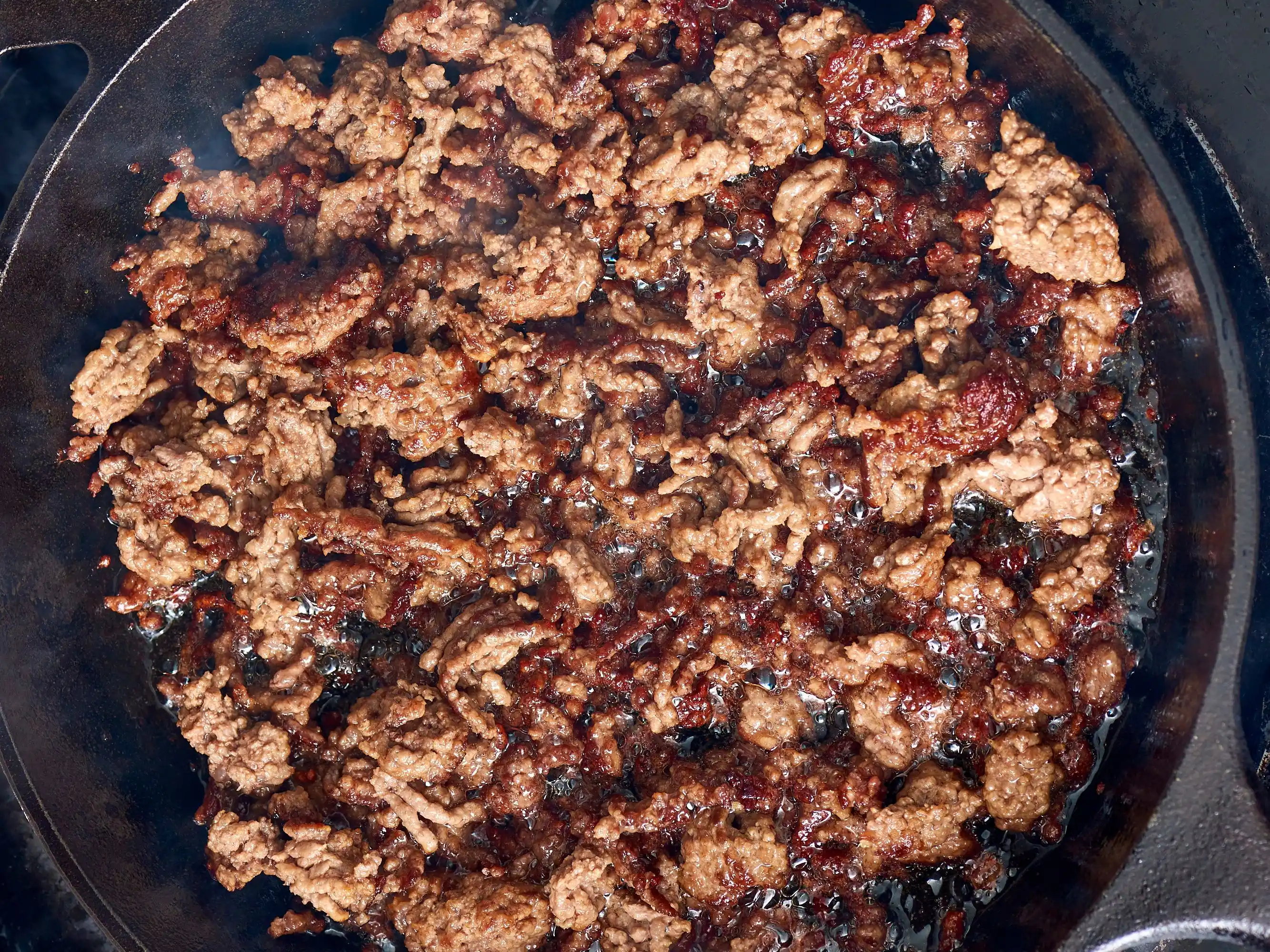 Ground beef browning in a skillet with crisp edges forming as a spatula breaks it into small crumbles