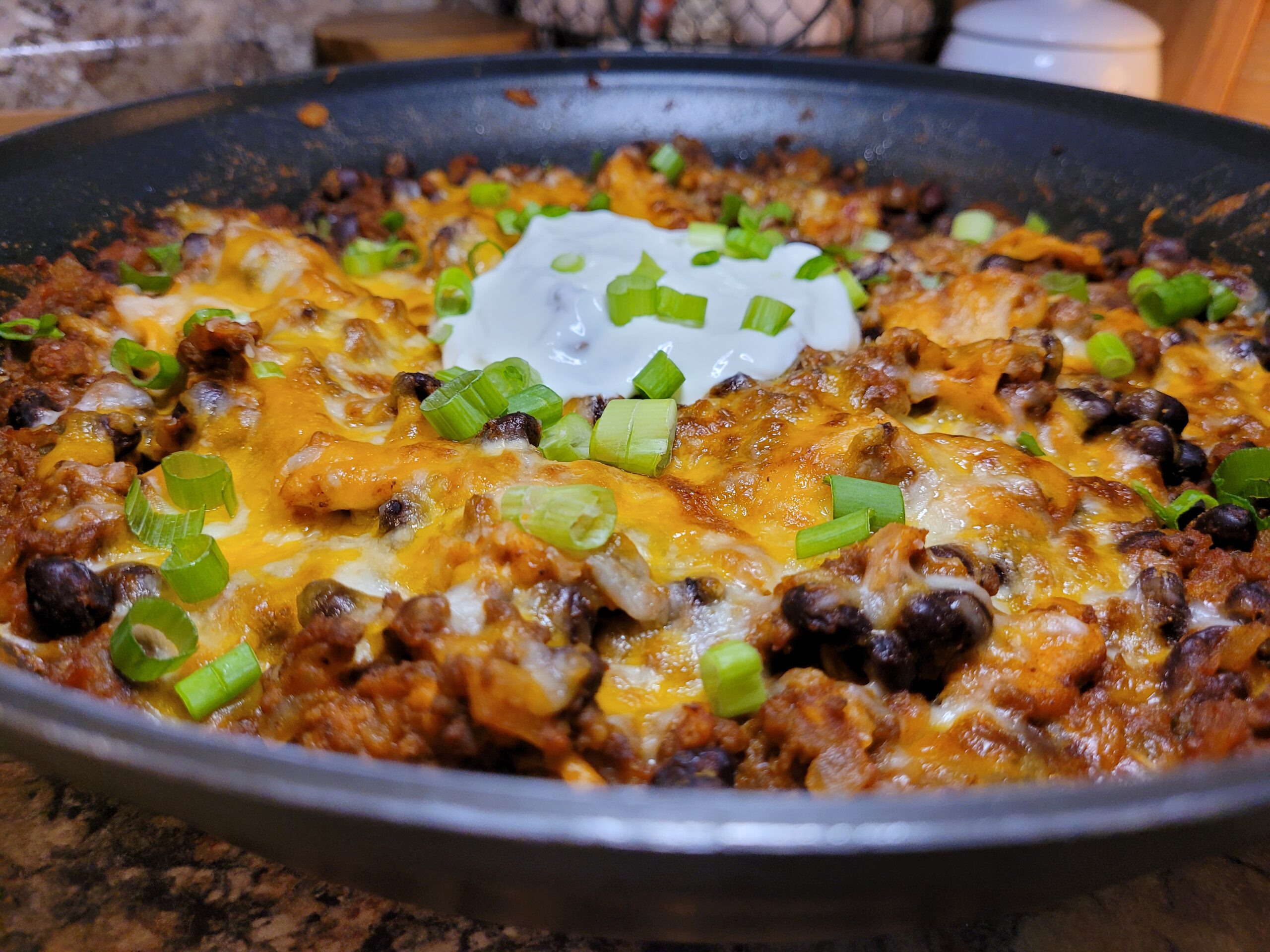 Ground beef browning in a skillet with diced onions and bell peppers, steam rising over a stovetop