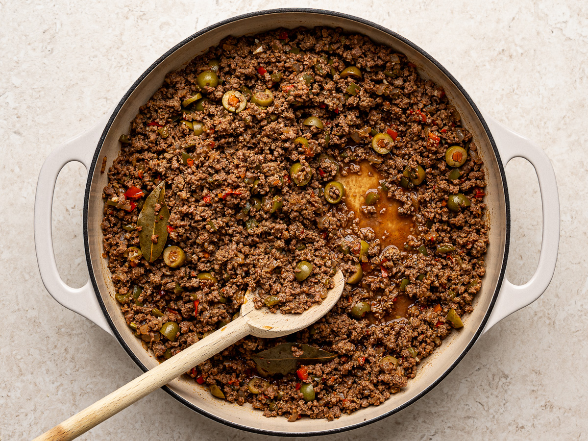 Ground beef empanada filling simmering in a skillet with onions and spices, thickened and glossy