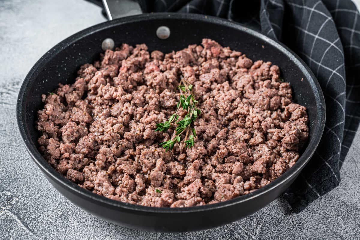 Ground pork and ground beef in bowls beside breadcrumbs, milk, grated onion, eggs, and seasonings on a kitchen counter