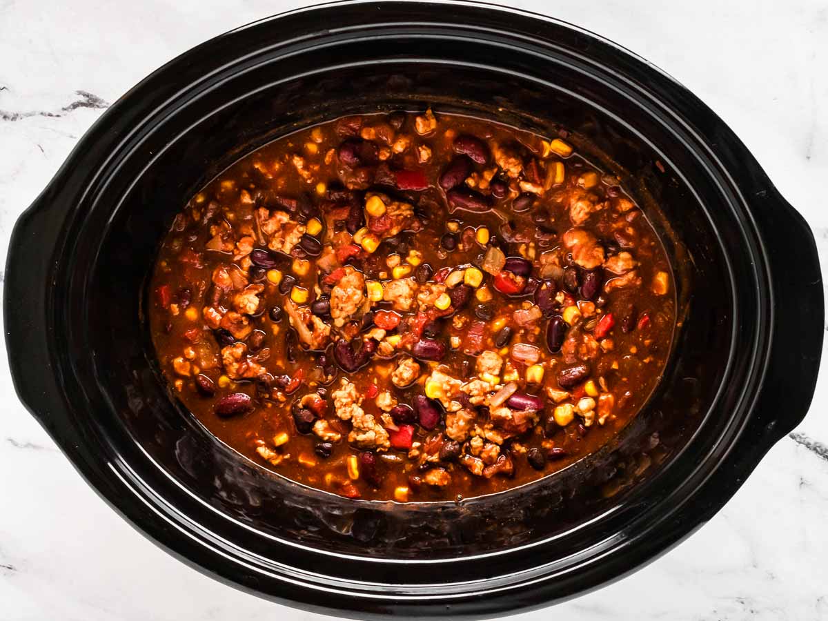 Ground turkey browning in a skillet with diced onions and minced garlic on a stovetop in a home kitchen