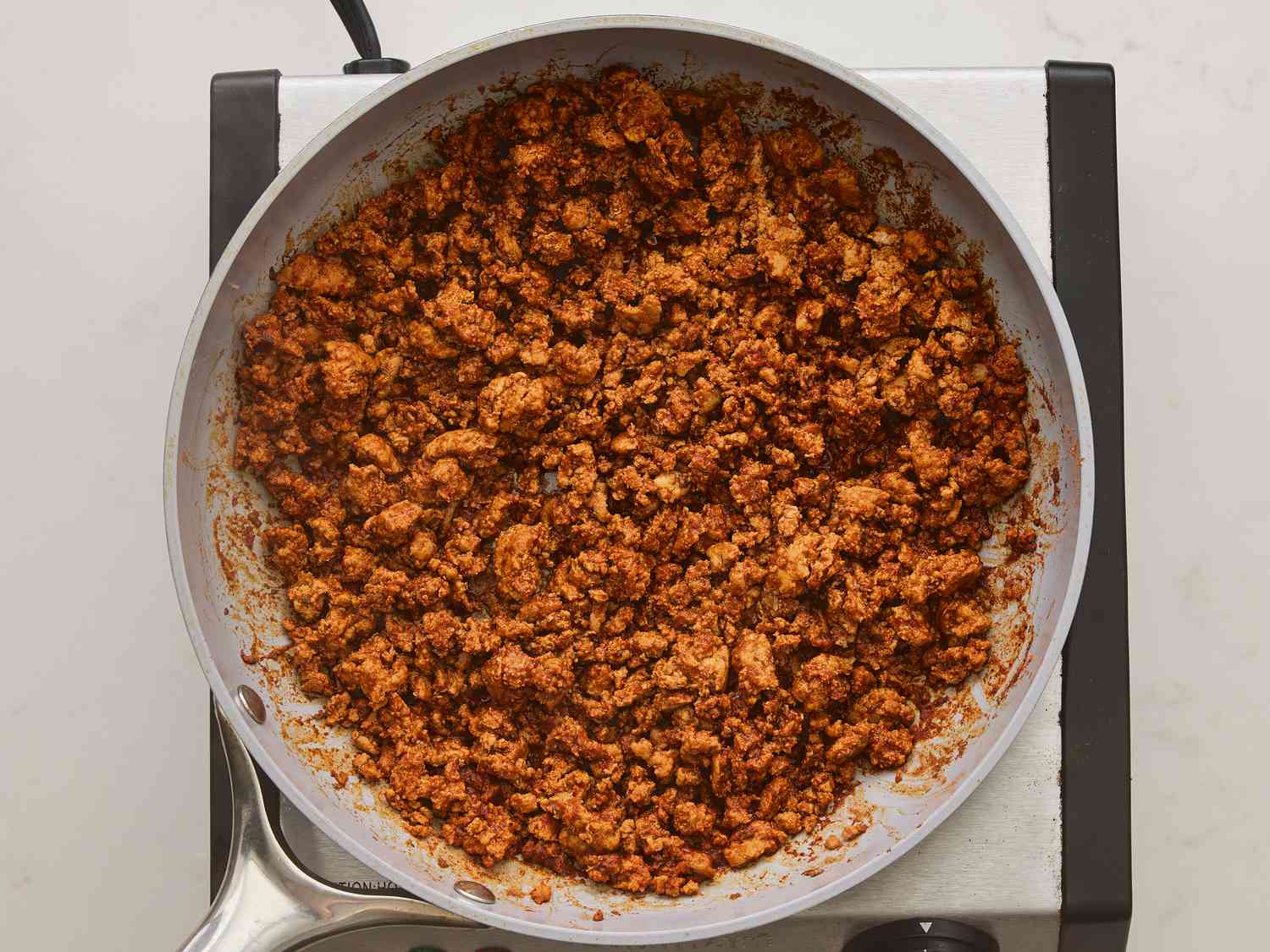 Ground turkey browning in a skillet with onions and peppers, being stirred with a wooden spoon on a stovetop