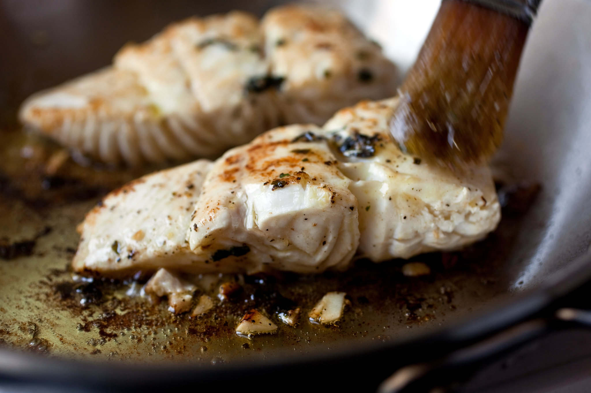 Halibut fillets being brushed with olive oil and sprinkled with salt and pepper on a cutting board in a bright home kitchen