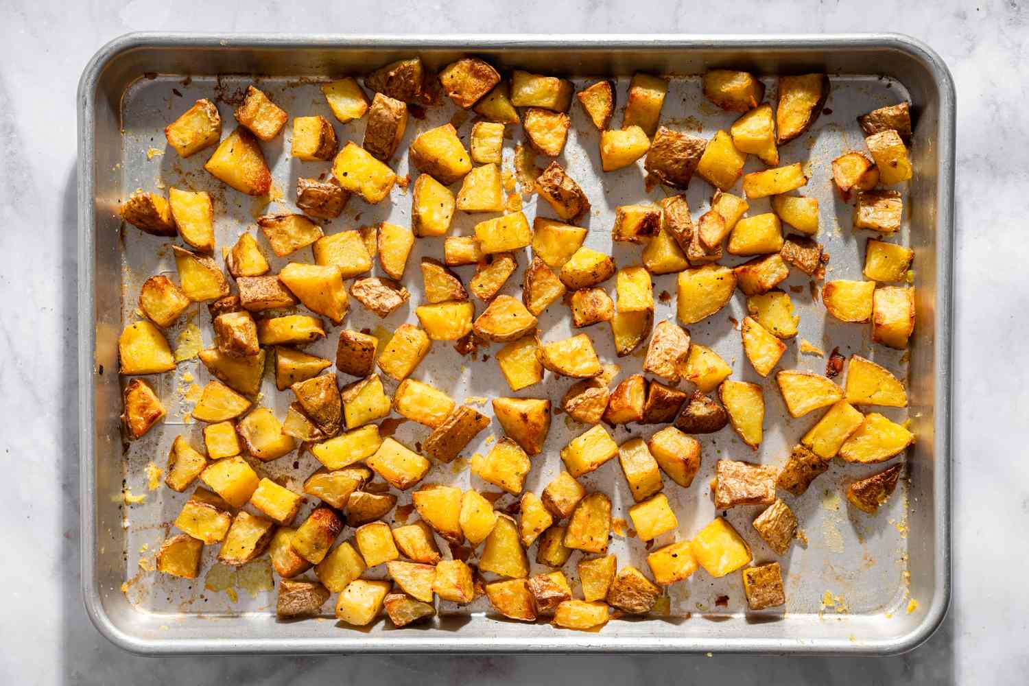 Halved baby potatoes cut-side down on a hot sheet pan going into the oven, golden light in a home kitchen