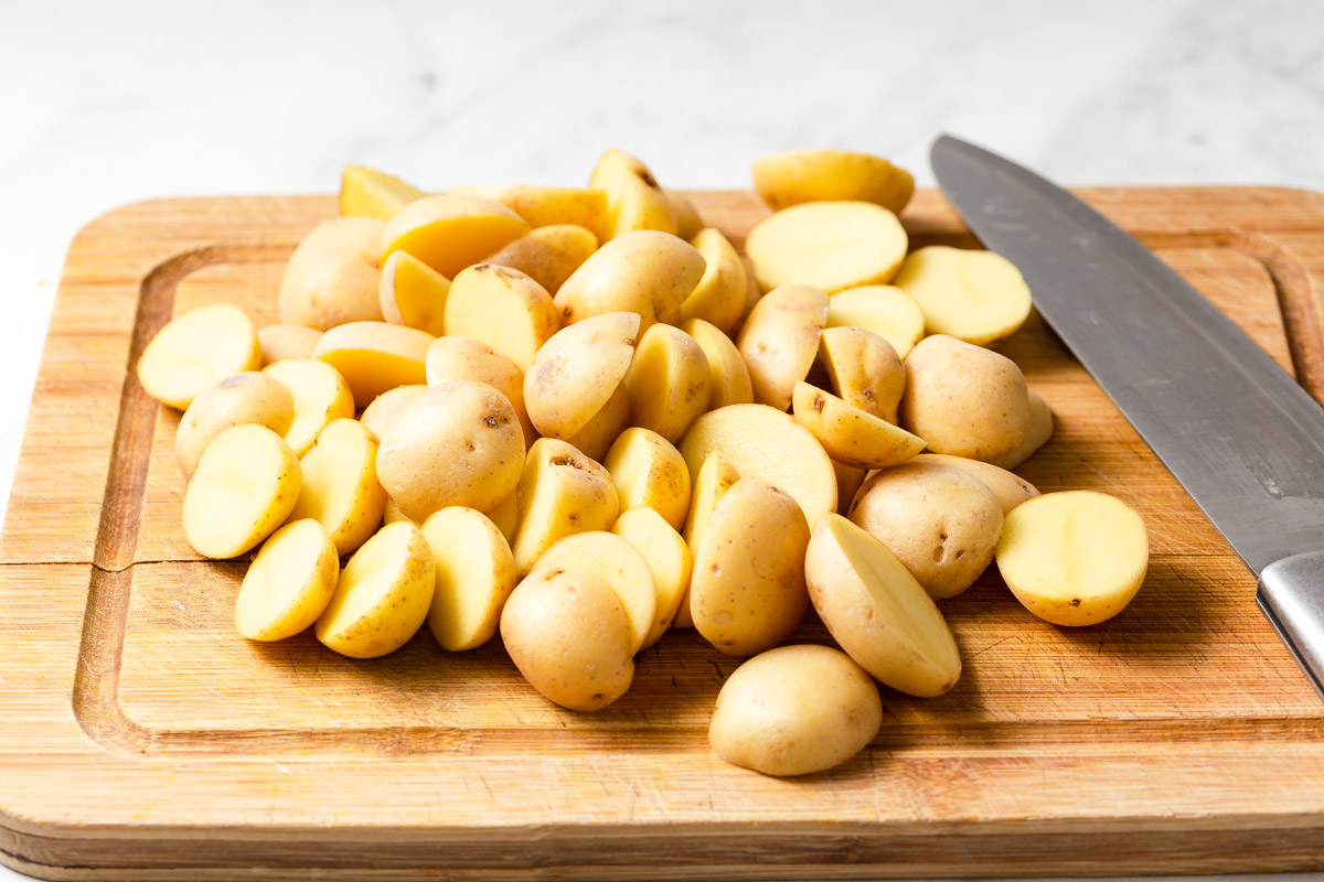 Halved baby potatoes scattered in a 9x13 baking pan with olive oil, salt, and pepper on a kitchen counter