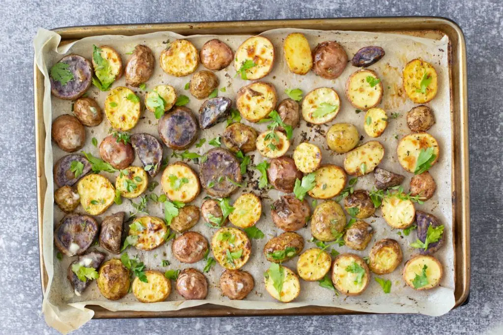 Halved baby potatoes spread on a parchment-lined sheet pan with olive oil and seasoning before going into the oven