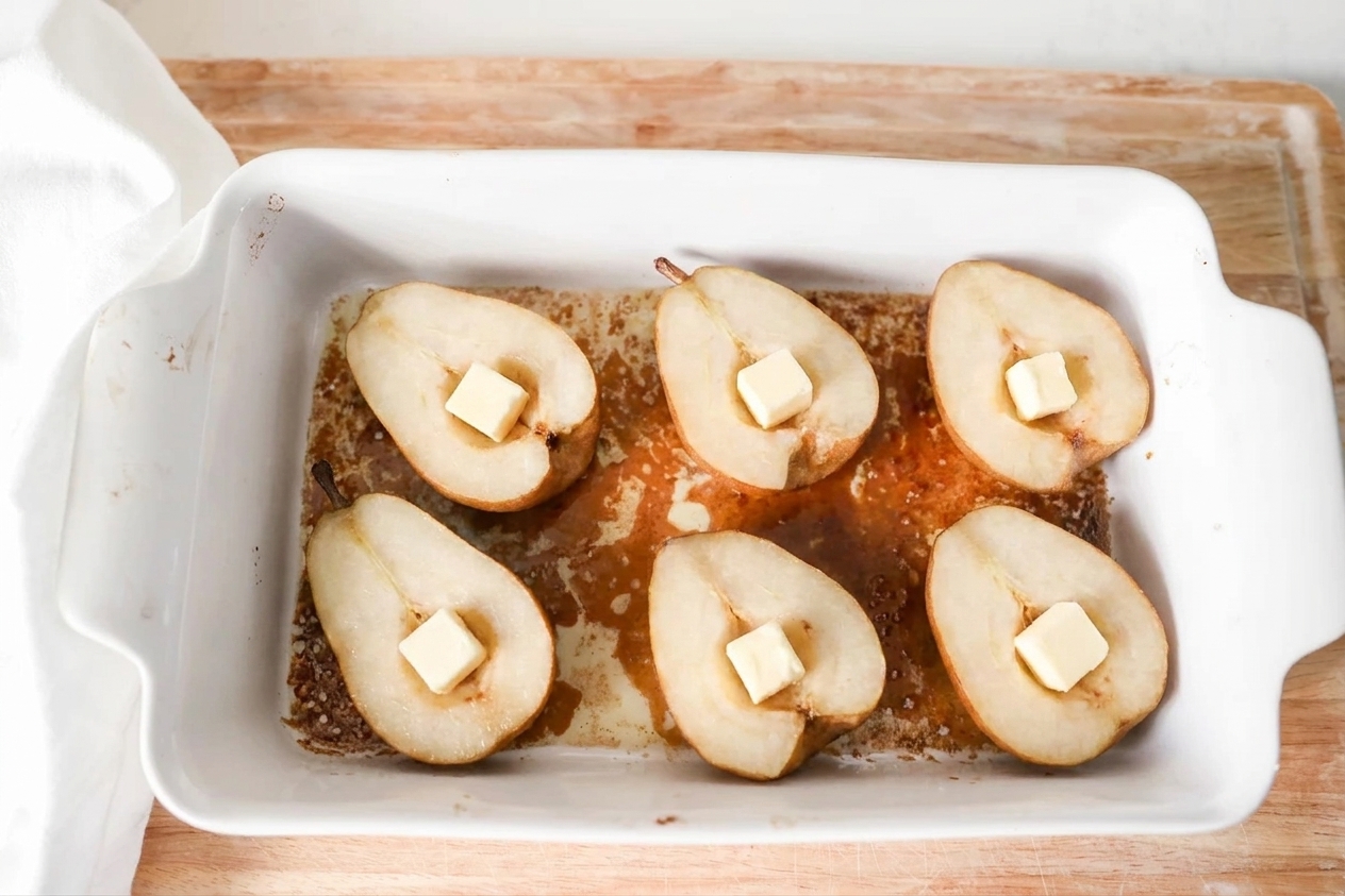 Halved pears arranged cut-side up in a baking dish with brown sugar sauce underneath and butter cubes tucked into the centers