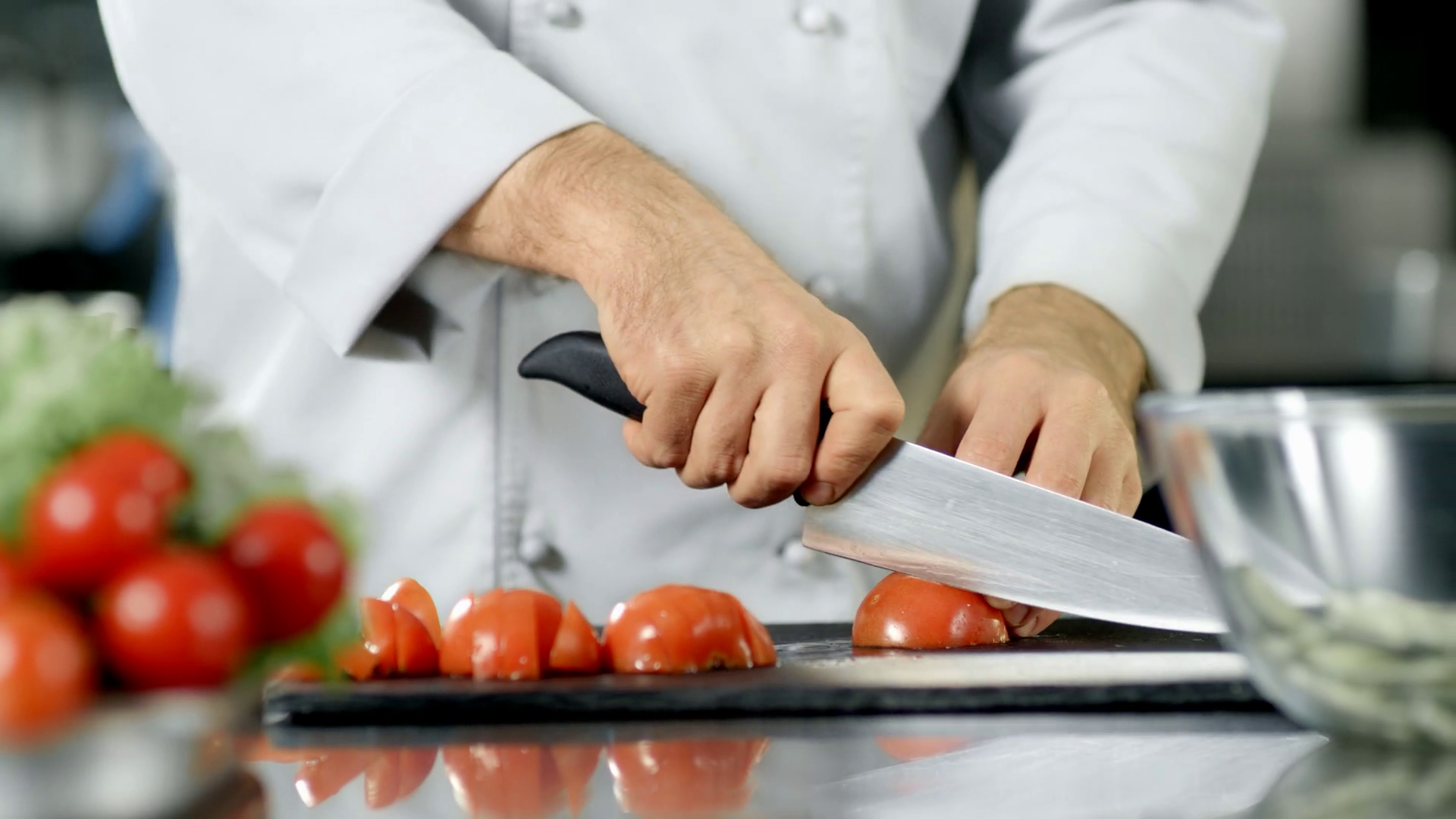 Hands chopping ripe tomatoes on a cutting board with a chef's knife, with onion and cilantro nearby