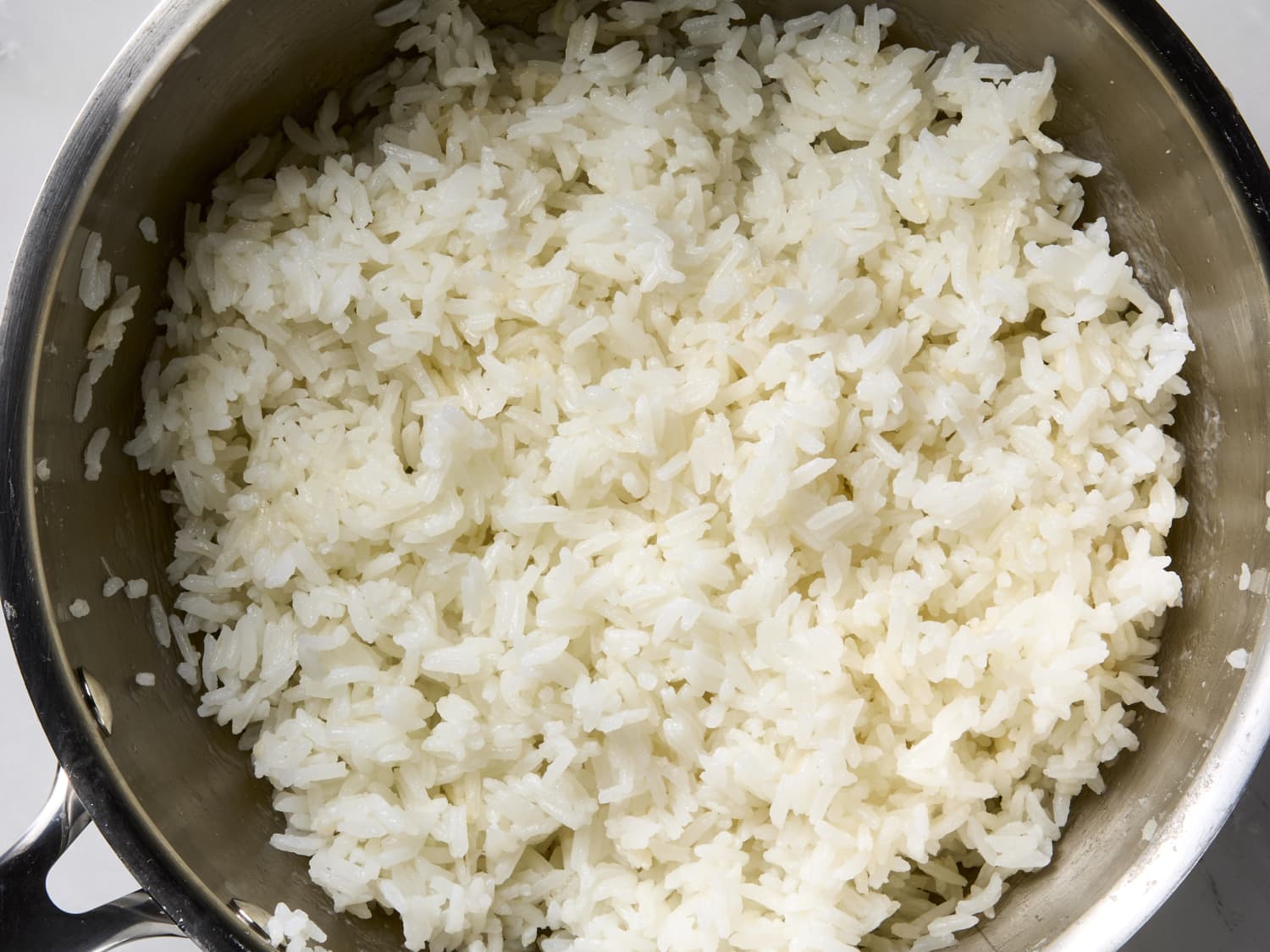 Hands fluffing and breaking up cold cooked jasmine rice in a large bowl on a kitchen counter