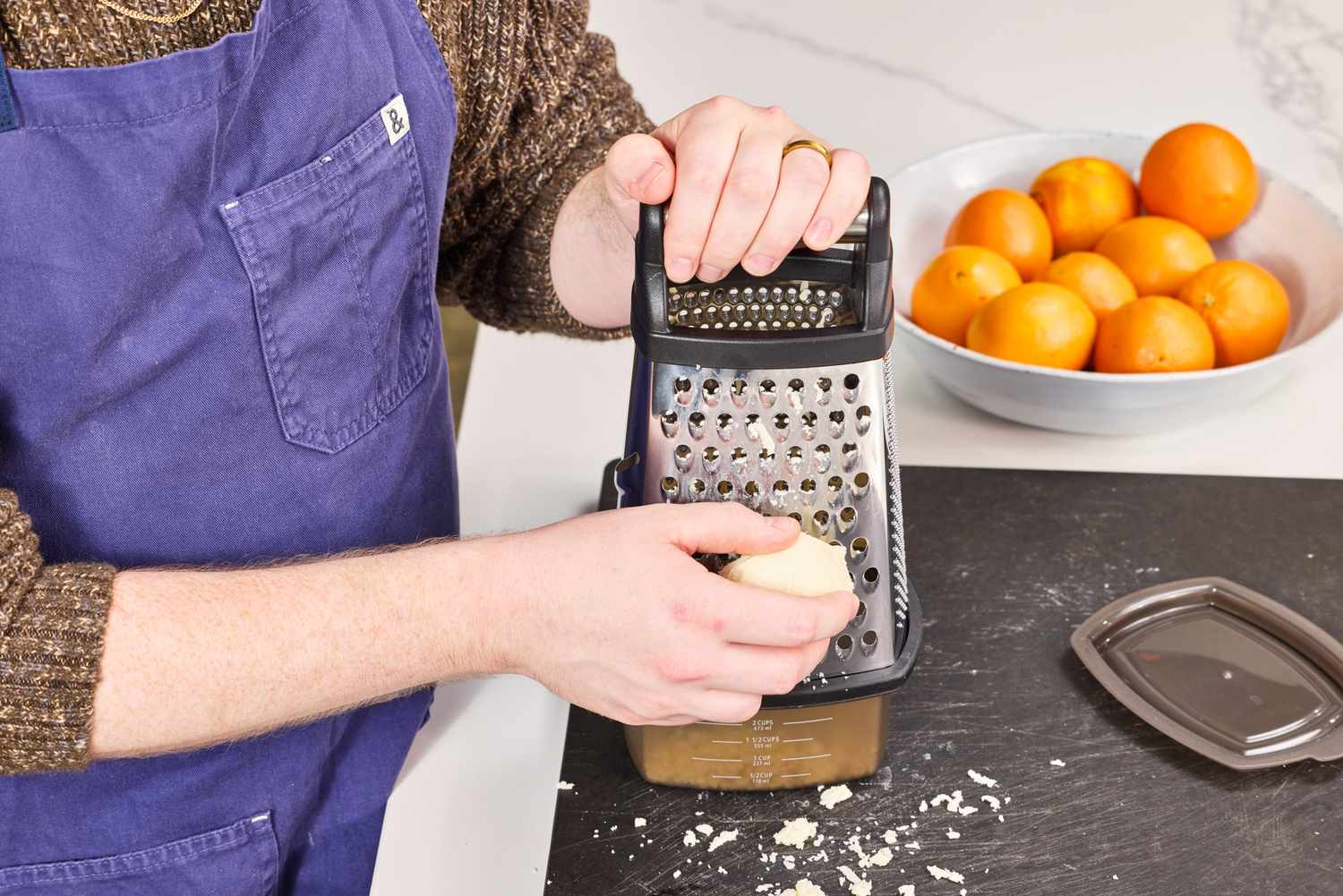 Hands grating a peeled russet potato on a box grater over a bowl on a home kitchen counter